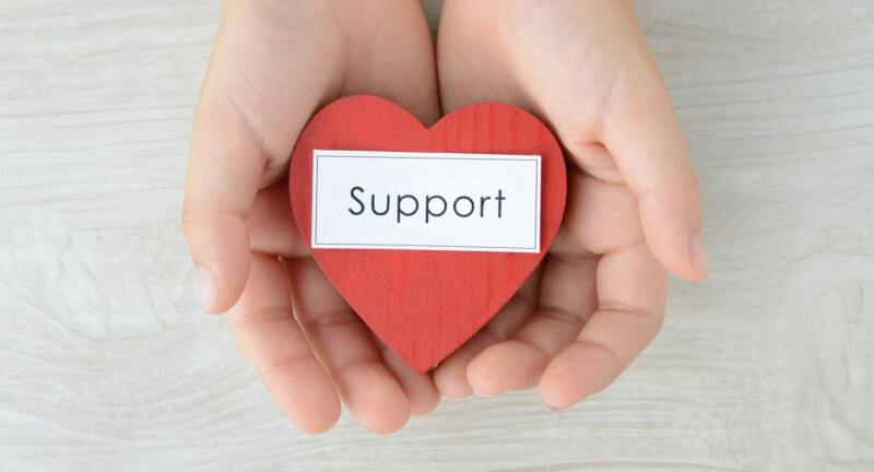 英語で「Support」と書かれたハート型の小物を両手で差し出す様子